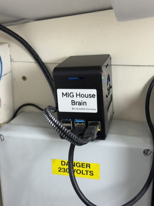 A Raspberry Pi in a black case mounted above the consumer unit, labelled MIG House Brain by HomeKit Harmony