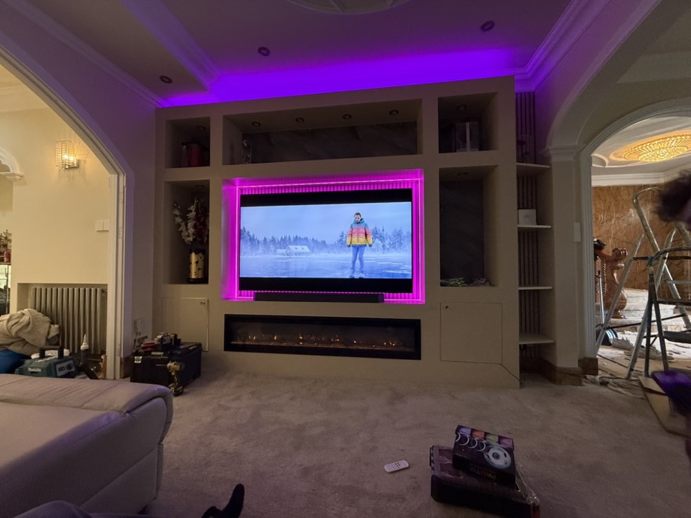 A finished media wall with a large television, magenta backlighting, cove lighting and a linear fireplace, in a large period room