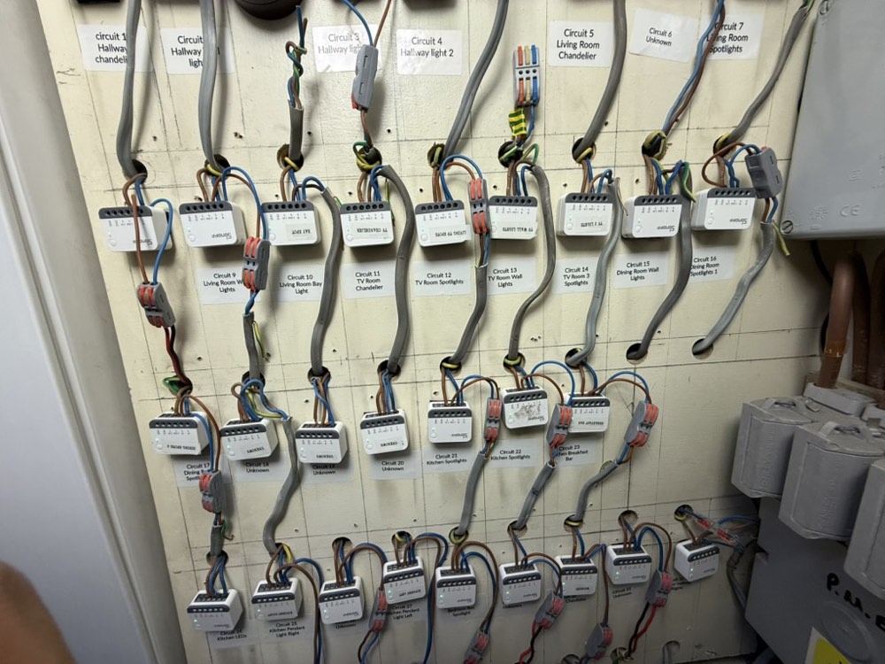The same wall rebuilt with white Zigbee relay modules, wired through lever connectors, each circuit labelled with the room it controls